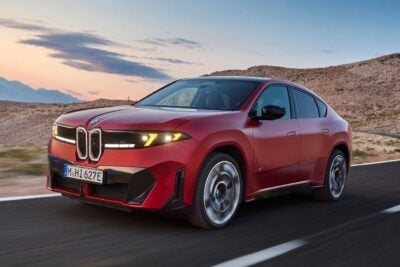 BMW iX3 M60 xDrive elektrikli SUV’nin dinamik bir sürüş sahnesi, yol kenarında hızlı şarj istasyonu