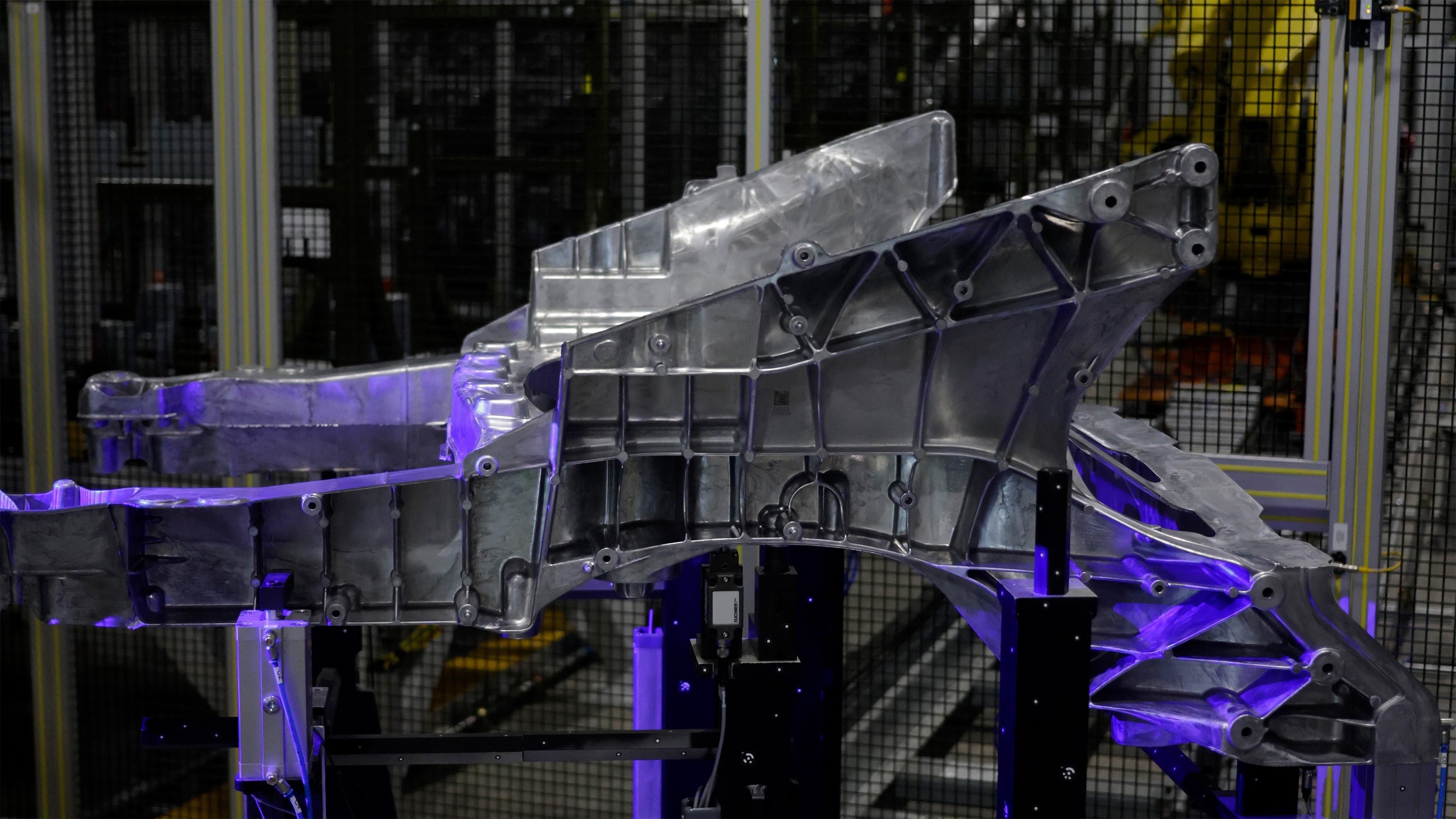 Büyük bir alüminyum döküm parçayı tutan bir robot kolun bulunduğu endüstriyel fabrika ortamı