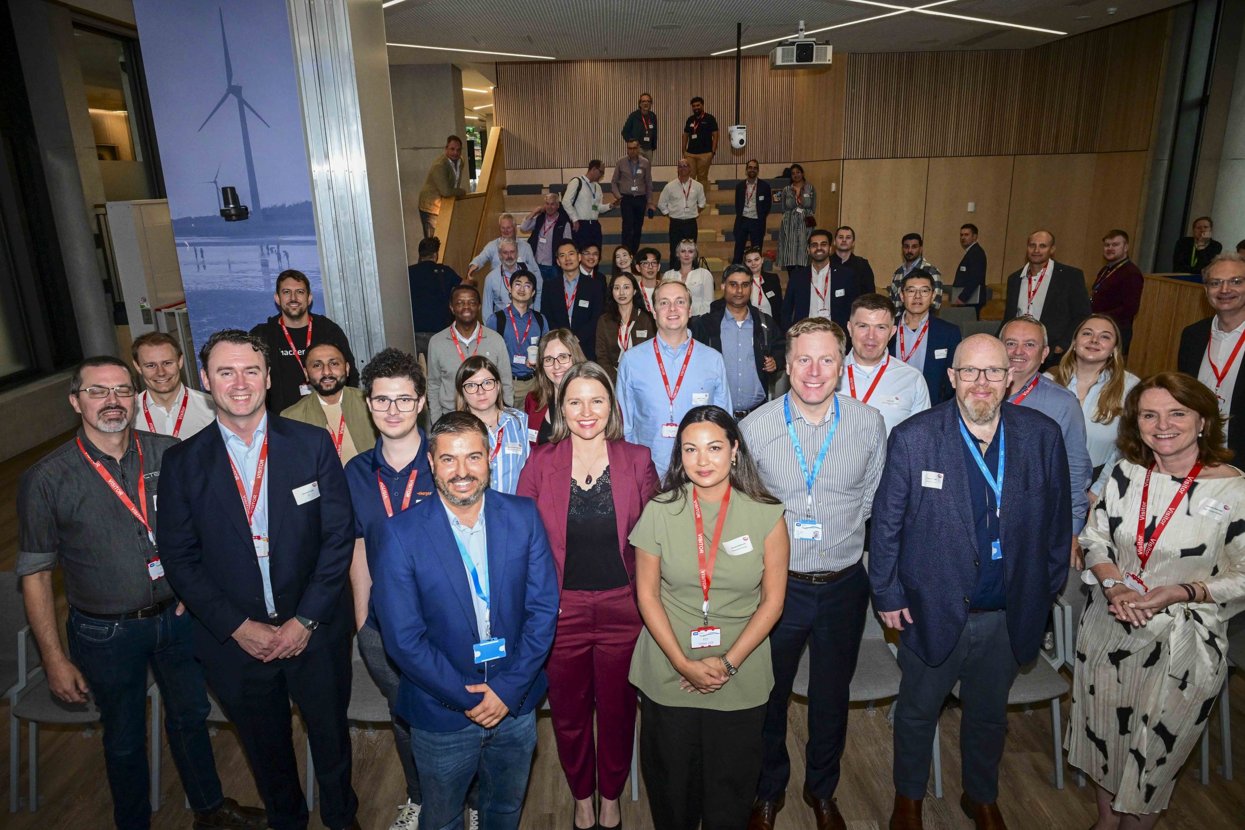 Dublin'deki bir konferans salonunda, OCPP Plugfest etkinliğinde katılımcıların şarj cihazları ve ekranlar etrafında test yaptığı bir sahne.