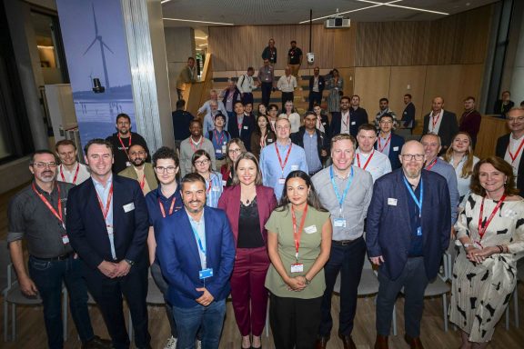 Dublin'deki bir konferans salonunda, OCPP Plugfest etkinliğinde katılımcıların şarj cihazları ve ekranlar etrafında test yaptığı bir sahne.