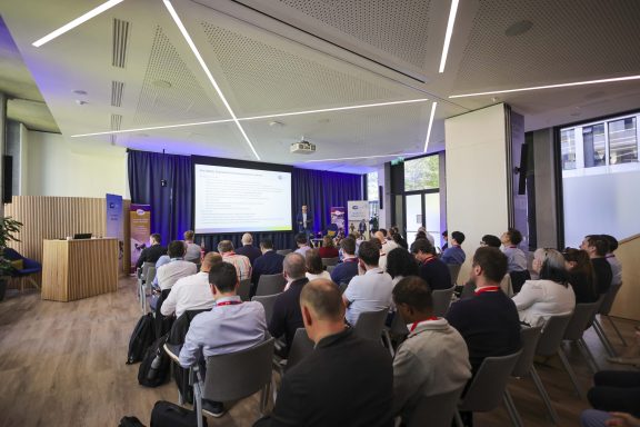 Dublin'deki bir konferans salonunda, OCPP Plugfest etkinliğinde katılımcıların şarj cihazları ve ekranlar etrafında test yaptığı bir sahne.