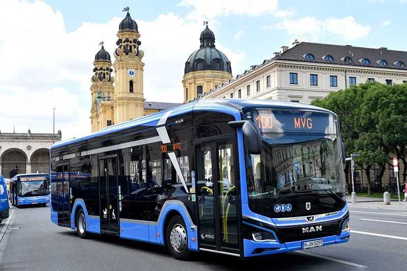 Almanya'da bir cadde üzerinde duran elektrikli şehir otobüsü, arka planda modern binalar ve yeşil alanlar