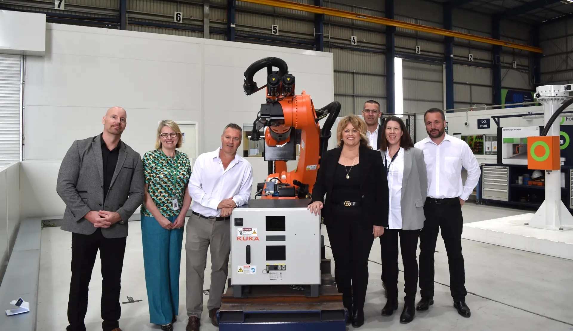 Avustralya'daki bir maden sahasında, dev bir elektrikli kamyonun yanında endüstriyel bir robot kolunun şarj kablosunu yönettiği sahne