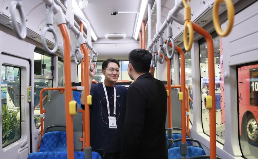 Singapur kent merkezinde modern bir elektrikli otobüs durağa yanaşırken, arka planda akıllı ulaşım altyapısı ve yolcu bilgilendirme ekranları görülüyor.