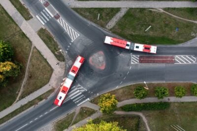 Hindistan'da bir otoyolda seyreden mavi-beyaz elektrikli şehirlerarası otobüs, arka planda yeşil tepeler ve güneşli bir gökyüzü.