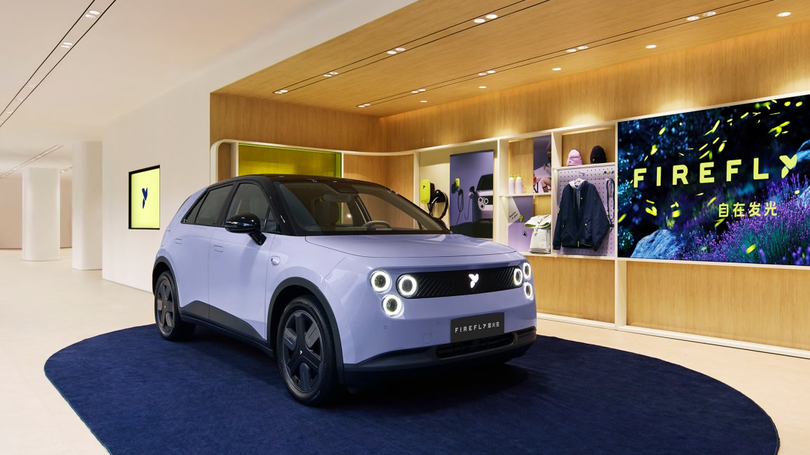 Nio Firefly kompakt elektrikli otomobilin yandan görünümü, parlak gün ışığı altında modern bir şehir caddesinde park halinde.