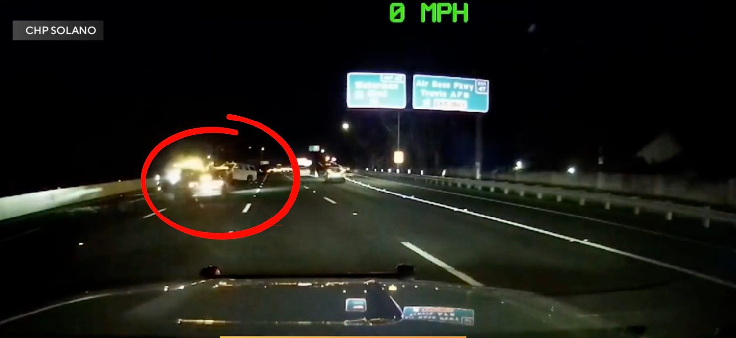 Gece otoyolda hasarlı bir Tesla sedan, polis aracına çarpmış, acil durum ışıkları yanıyor, polis memurları ve sağlık ekipleri çevrede.