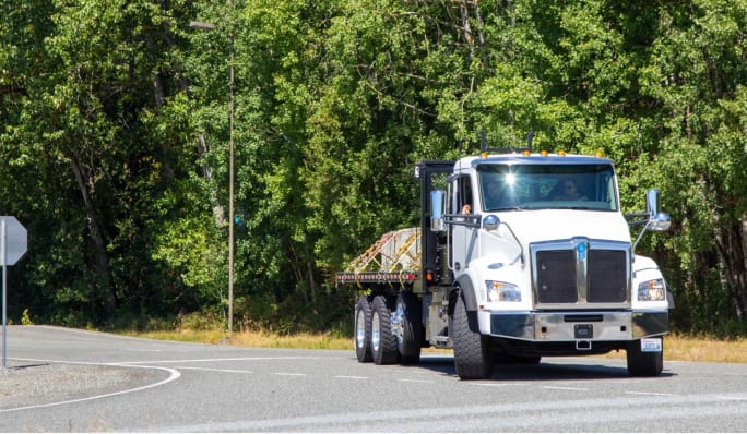 Kenworth T880E elektrikli kamyon, bir şantiye alanında DC hızlı şarj cihazına bağlı duruyor.