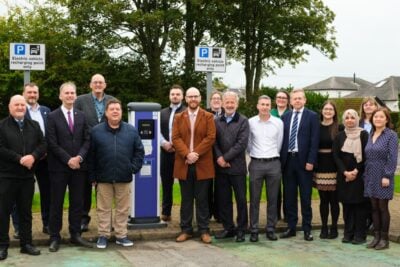 Bir lamba direğine monte edilmiş kuş yuvası şeklinde ödeme terminali ve yanında elektrikli araç şarj istasyonu, gündüz, açık hava